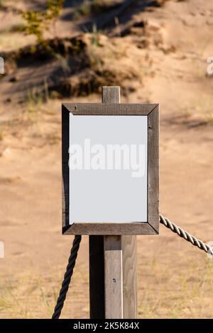 Cartello bianco vuoto con cornice in legno parzialmente spezzata su una spiaggia sabbiosa Foto Stock
