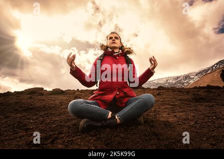 Donna escursionista seduta sulla pietra lavica pratica yoga in cima alla montagna - caldo filtro tramonto - persone e vagabondo stile di vita concetto Foto Stock