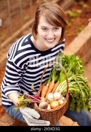 Fiero del suo raccolto. Giovane donna sorridente seduta con il suo cesto di verdure appena raccolte. Foto Stock