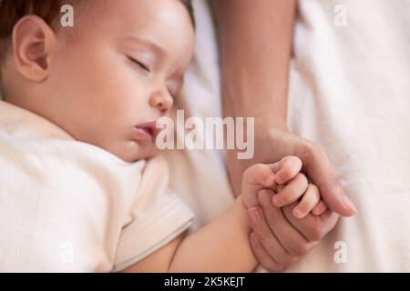 La mamma è sempre lì, anche nei miei sogni. Una bambina dorme mentre tiene la mano delle madri. Foto Stock