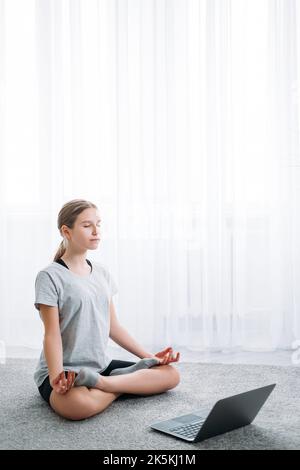 yoga online bambini casa meditazione ragazza con notebook Foto Stock