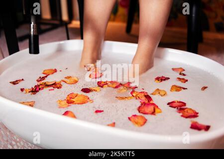 piedi femminili messi in un secchio per una pedicure Foto Stock