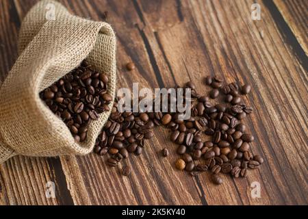 Chicchi di caffè in sacchetto di iuta e cucchiaio di legno sul tavolo Foto Stock