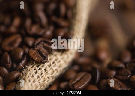 Chicchi di caffè in sacchetto di iuta e cucchiaio di legno sul tavolo Foto Stock