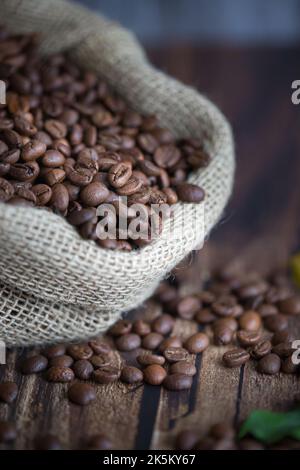 Chicchi di caffè in sacchetto di iuta e cucchiaio di legno sul tavolo Foto Stock