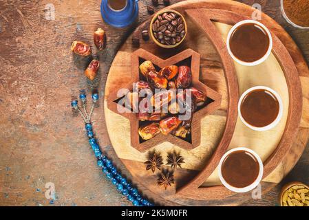 Tazze di caffè turche con chicchi di caffè tostati, datteri freschi e perle di rosario su sfondo rustico. Vista dall'alto con spazio di copia. Foto Stock