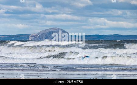 Un surfista nel Firth of Forth in una giornata ventosa con grandi onde con l'isola di Bass Rock in lontananza, Scozia, Regno Unito Foto Stock
