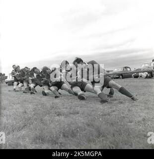 1964, storico, fuori in un campo, in maglia di rugby e shorts, calze lunghe e stivali hub-nail, una squadra di uomini che gareggiano in un concorso di tiro di guerra a Brill, Bucks, Inghilterra, UK. Foto Stock