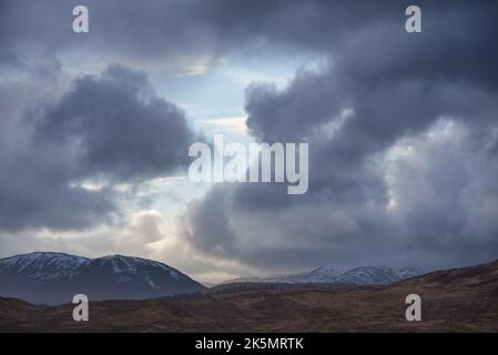 Un'immagine spettacolare del paesaggio dei cieli tempestosi sulle montagne innevate delle Highlands scozzesi Foto Stock