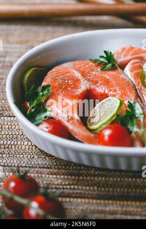 Bistecche di salmone fresco con lime, pomodori ciliegini, prezzemolo e olio d'oliva. Cena sana o pranzo concetto. Foto Stock