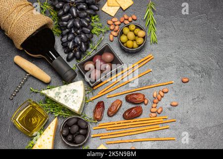 Aperitivo con vino rosso, olive e formaggio, uva e datteri, baguette e cracker, noci e rametti di timo. Spazio di copia. Giacitura piatta. Bla Foto Stock