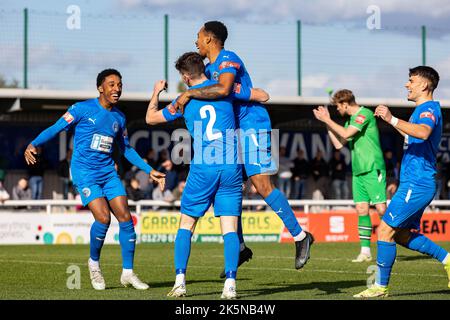 Una squadra di calcio festeggia dopo aver segnato un gol, mentre un giocatore di opposizione applaude il linesman Foto Stock