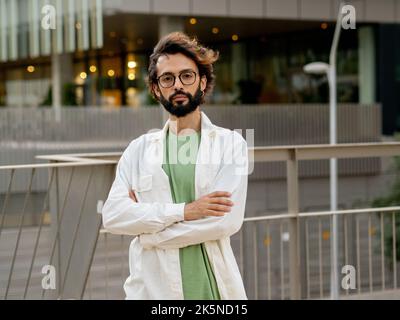 Giovane imprenditore digitale che guarda seriamente alla fotocamera di una città. Giovane uomo d'affari millenario Foto Stock