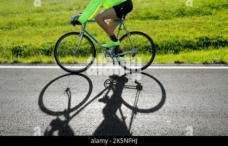 il ciclista corre veloce contro la luce con una storica bici da corsa sulla strada asfaltata Foto Stock