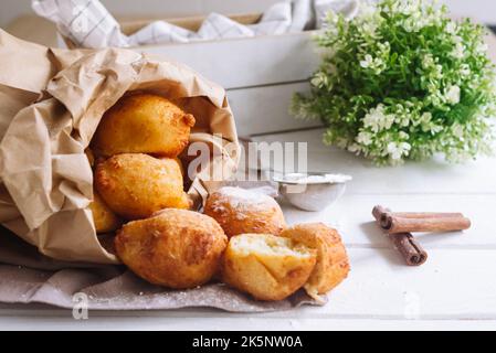 Ricotta formaggio rotondo ciambelle mucchio con zucchero a velo in un sacchetto di carta. Palle di pasta intere senza fori. Foto Stock