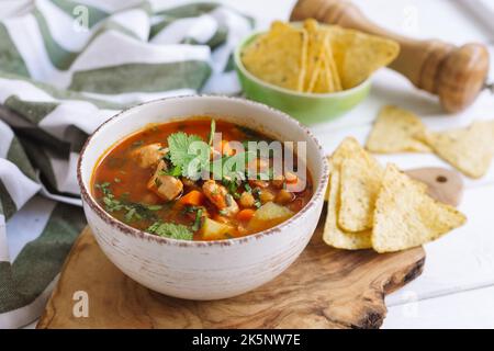 Zuppa densa con pollo, fagioli e verdure, ceci e nachos. Quasi peperoncino. Casalinghi, confortante e sostanzioso pasto caldo in una profonda ciotola di ceramica. Foto Stock