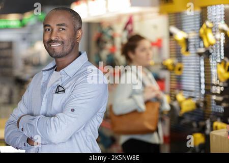 addetto alle vendite del negozio di hardware in piedi accanto agli scaffali Foto Stock