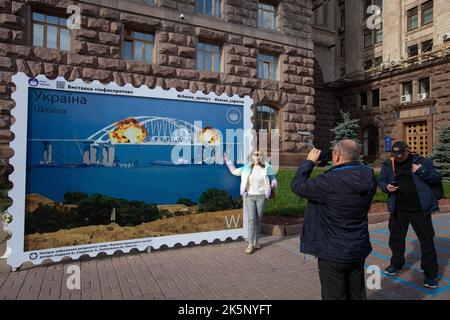 Kiev, Ucraina. 9th Ott 2022. Le persone sono fotografate con un modello di francobollo che raffigura il ponte di Crimea in fiamme sullo sfondo, nel centro di Kyiv. Il 8 ottobre si verificò un'esplosione sul ponte di Crimea costruito in Russia che collegava la Russia e la penisola di Crimea da essa occupata, danneggiando parte della struttura del ponte. (Credit Image: © Oleksii Chumachenko/SOPA Images via ZUMA Press Wire) Credit: ZUMA Press, Inc./Alamy Live News Foto Stock