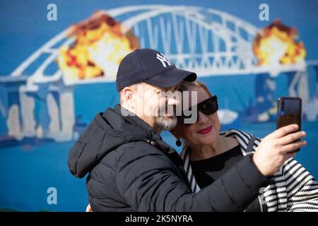 Kiev, Ucraina. 9th Ott 2022. Le persone sono fotografate con un modello di francobollo che raffigura il ponte di Crimea in fiamme sullo sfondo, nel centro di Kyiv. Il 8 ottobre si verificò un'esplosione sul ponte di Crimea costruito in Russia che collegava la Russia e la penisola di Crimea da essa occupata, danneggiando parte della struttura del ponte. (Credit Image: © Oleksii Chumachenko/SOPA Images via ZUMA Press Wire) Credit: ZUMA Press, Inc./Alamy Live News Foto Stock