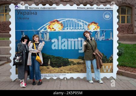 Kiev, Ucraina. 9th Ott 2022. La gente posa per una foto con un modello di timbro che raffigura il ponte di Crimea in fiamme sullo sfondo, nel centro di Kyiv. Il 8 ottobre si verificò un'esplosione sul ponte di Crimea costruito in Russia che collegava la Russia e la penisola di Crimea da essa occupata, danneggiando parte della struttura del ponte. (Credit Image: © Oleksii Chumachenko/SOPA Images via ZUMA Press Wire) Credit: ZUMA Press, Inc./Alamy Live News Foto Stock