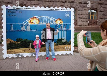 Kiev, Ucraina. 9th Ott 2022. La gente posa per una foto con un modello di timbro che raffigura il ponte di Crimea in fiamme sullo sfondo, nel centro di Kyiv. Il 8 ottobre si verificò un'esplosione sul ponte di Crimea costruito in Russia che collegava la Russia e la penisola di Crimea da essa occupata, danneggiando parte della struttura del ponte. (Credit Image: © Oleksii Chumachenko/SOPA Images via ZUMA Press Wire) Credit: ZUMA Press, Inc./Alamy Live News Foto Stock