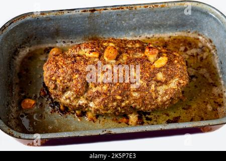 Polpettone di manzo intero cotto al forno con aglio e cipolla in vecchia padella rurale, spicchio. Foto Stock