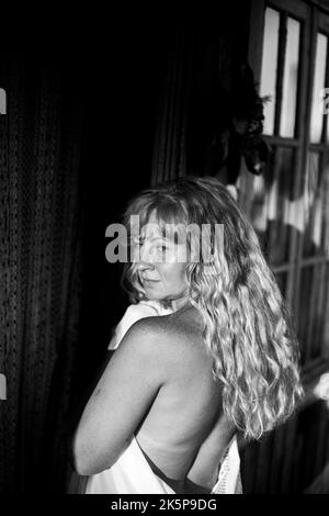 Ritratto di una donna dai capelli lunghi avvolta in un asciugamano all'esterno di una casa di campagna. Foto in bianco e nero. Foto Stock
