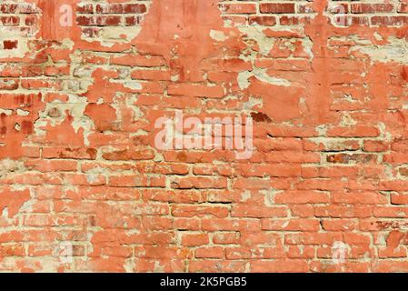 Un vecchio muro di mattoni rossi in parte ricoperto di intonaco rosso, in parte i mattoni sono esposti, visibili. Foto Stock