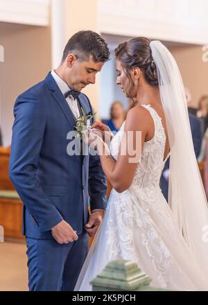 Sposa mette una decorazione floreale sul petto di una bgroom durante una cerimonia di nozze. Foto Stock