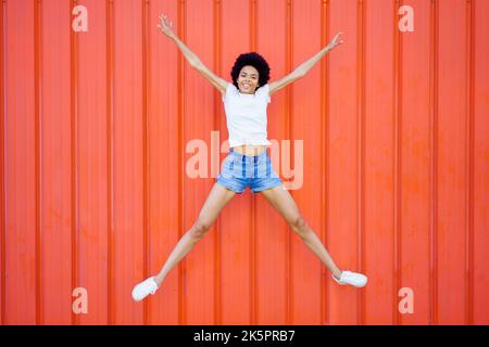 Donna nera gioiosa che salta vicino al muro Foto Stock