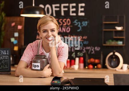 Giovane barista femminile con barattolo al tavolo nel bar Foto Stock