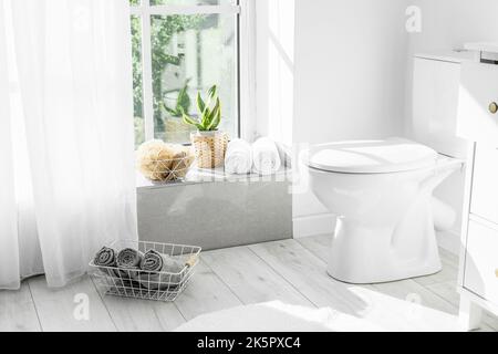 Moderna tazza di gabinetto e asciugamani vicino alla finestra all'interno del bagno Foto Stock