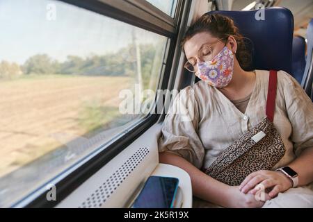 Una ragazza con gli occhiali in una maschera medica che dorme sul treno Foto Stock