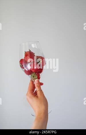 Bicchiere da vino femminile con fragole fresche sulla parete bianca. Foto Stock