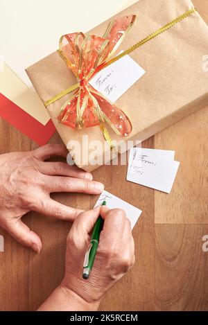 Donna matura irriconoscibile che scrive, facendo le schede fatte a mano per mettere sui suoi regali di Natale. Composizione vista dall'alto con spazio di copia. Foto Stock