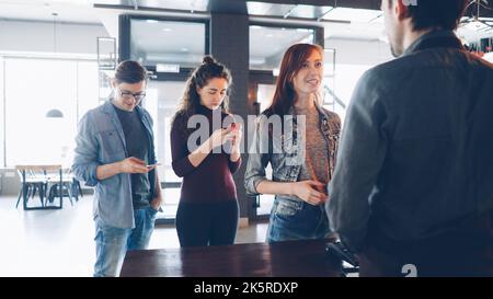 Coda di giovani allegri in piedi in casa del caffè la mattina e l'acquisto di bevande da asporto . Stile di vita moderno. Foto Stock