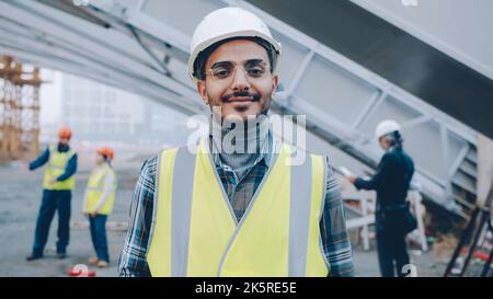 Ritratto del giovane costruttore mediorientale che indossa uniforme in piedi in cantiere sorridendo e guardando la macchina fotografica. Persone e concetto di occupazione. Foto Stock