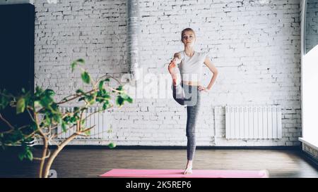 Iniziare studente di yoga femminile sta facendo una sequenza di esercizi di equilibrio in una classe di yoga uno-a-uno in un bel studio. A volte è scomoda, ma sta facendo buoni progressi. Apprendimento del concetto di yoga. Foto Stock