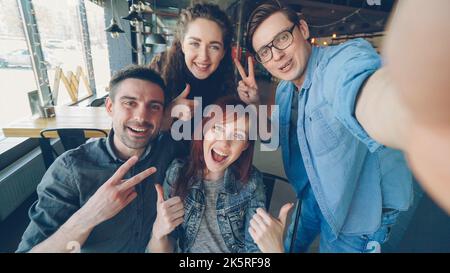 Punto di vista scatto di amici allegri che prendono selfie in pizzeria posa e sorridente, ridendo e gesturing insieme. Concetto di amicizia e di giovani felici. Foto Stock