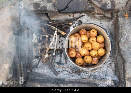 Campfire mele al forno. Tradizionale mela cucina in un calderone di ghisa sul fuoco in campeggio. Mele al forno sul falò. Vista dall'alto Foto Stock