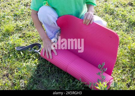 Donna con tappetino rosa yoga su sfondo verde erba nel parco. Concetto di salute e fitness. Foto Stock