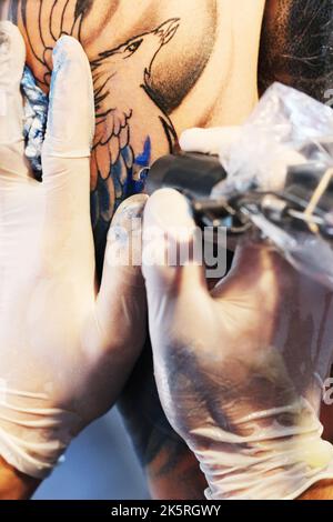 Decorazione cutanea. Artista tatuaggio occupato a riempire i contorni di un uccello con inchiostro blu su un braccio clienti. Foto Stock