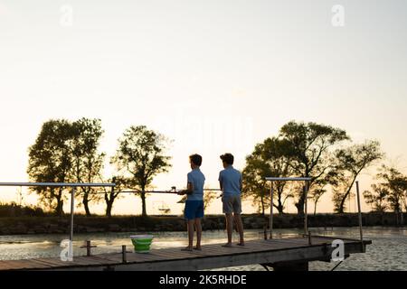 i bambini con canne da pesca si trovano su un molo di legno e pescano sul lago. Pesca Foto Stock