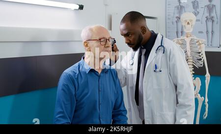 Medico di sesso maschile che fa consultazione con l'orecchio strumento otoscopio, controllo infezione con strumento di otologia a appuntamento medico. Otolaringologo che esegue un esame di otologia ent con un paziente anziano. Foto Stock
