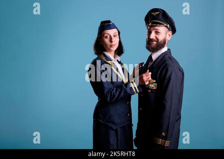 Sorridente pilota di aeroplano e assistente di volo coppia in uniforme guardando la macchina fotografica, studio medio scatto ritratto. Equipaggio di aerei, capitano di aerei e hostess aereo in piedi, equipaggio di aerei Foto Stock