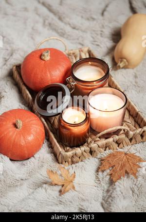 Vassoio di vimini con candele e zucche su una coperta calda. Decorazioni per le vacanze autunnali per la casa. Accogliente concetto autunnale. Foto Stock