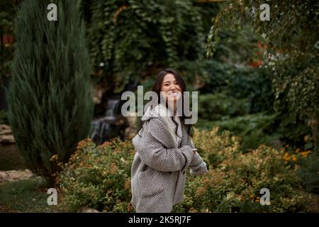 Primo piano ritratto di bella bella donna asiatica kazako brunetta in camice con sorriso affascinante camminando all'aperto nel parco. Faccia felice. Autunno Foto Stock