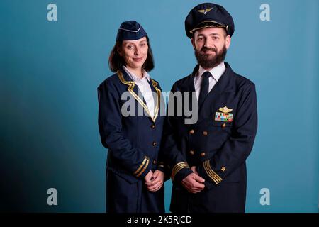 Pilota sorridente di aeroplano e assistente di volo in uniforme professionale studio medio ritratto scatto, l'equipaggio di aeroplano che guarda la macchina fotografica. Capitano aereo e hostess aereo in piedi, aircrew Foto Stock