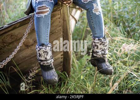 Donna africana con jeans moderni indossati siede su una vecchia barca di legno in autunno svedese Foto Stock