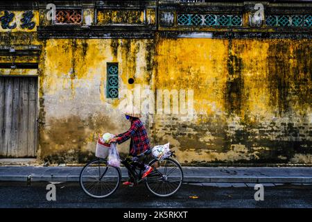 Una ciclista femminile corre in bicicletta lungo la strada nella città vecchia di Hoi An, Vietnam. Foto Stock